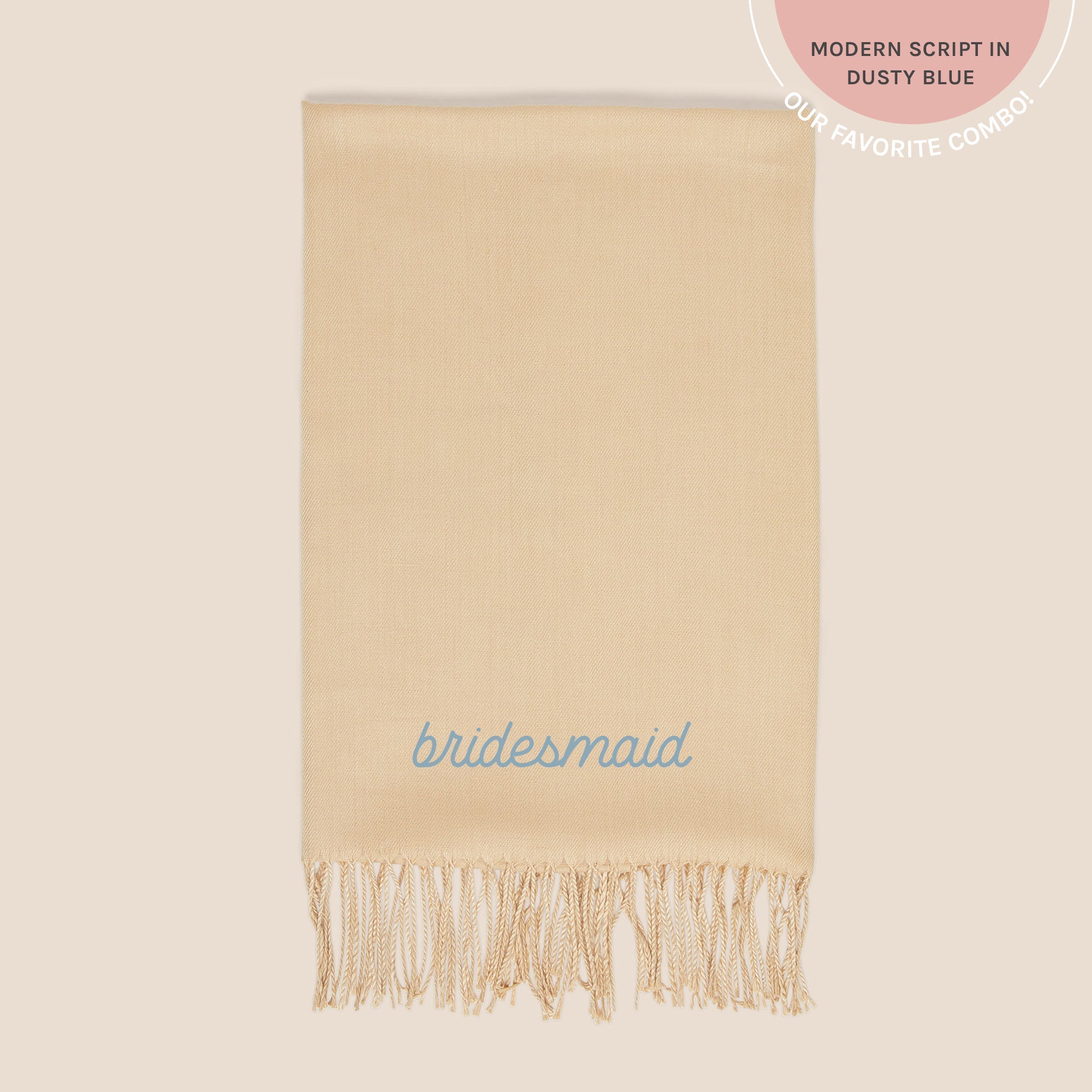 Flat view of the Shawl with Fringe in beige folded into a rectangle and embroidered the word 