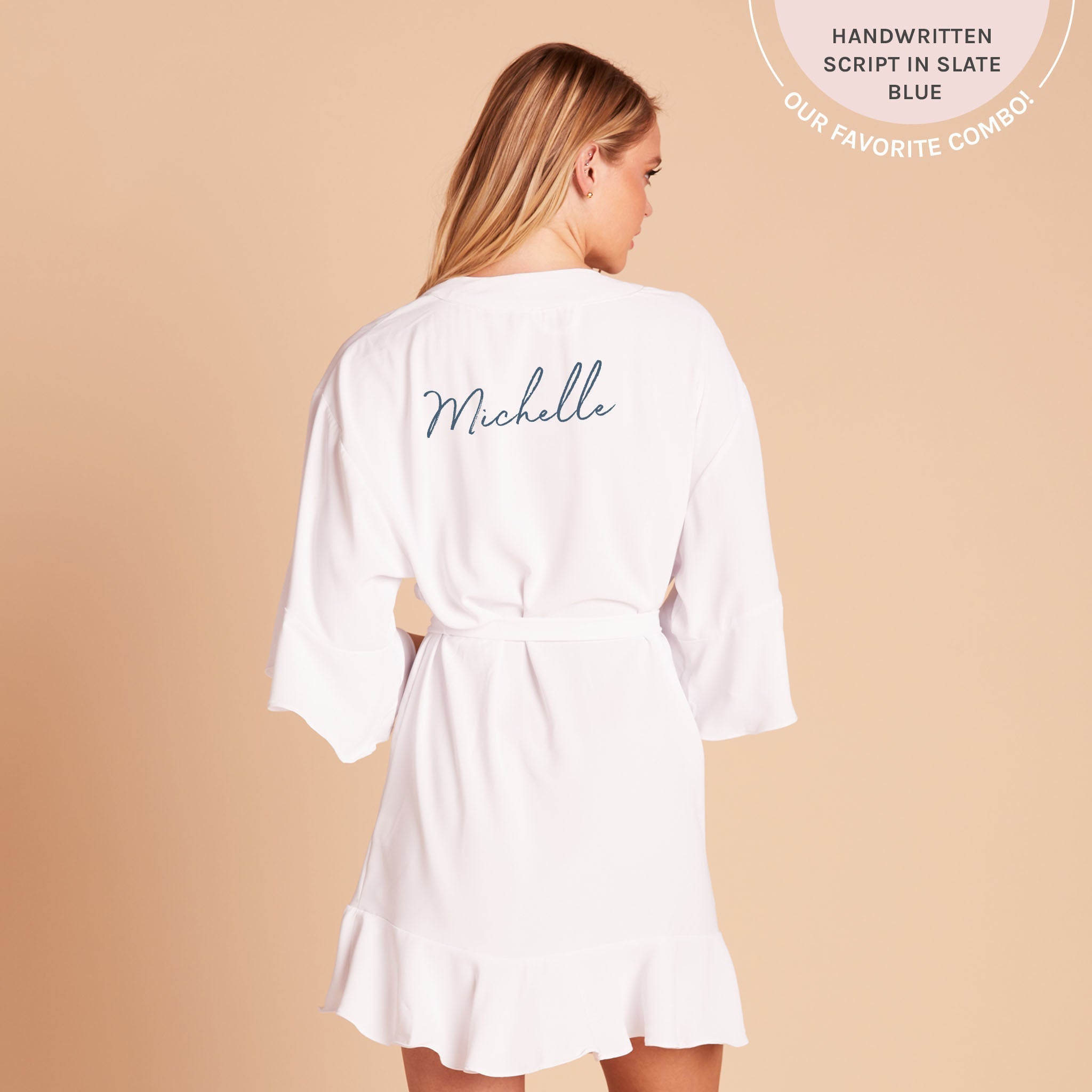 Back view of the Kenny Ruffle Robe in white shows a slender model with a light skin tone with the robe tied around the waist. The name 