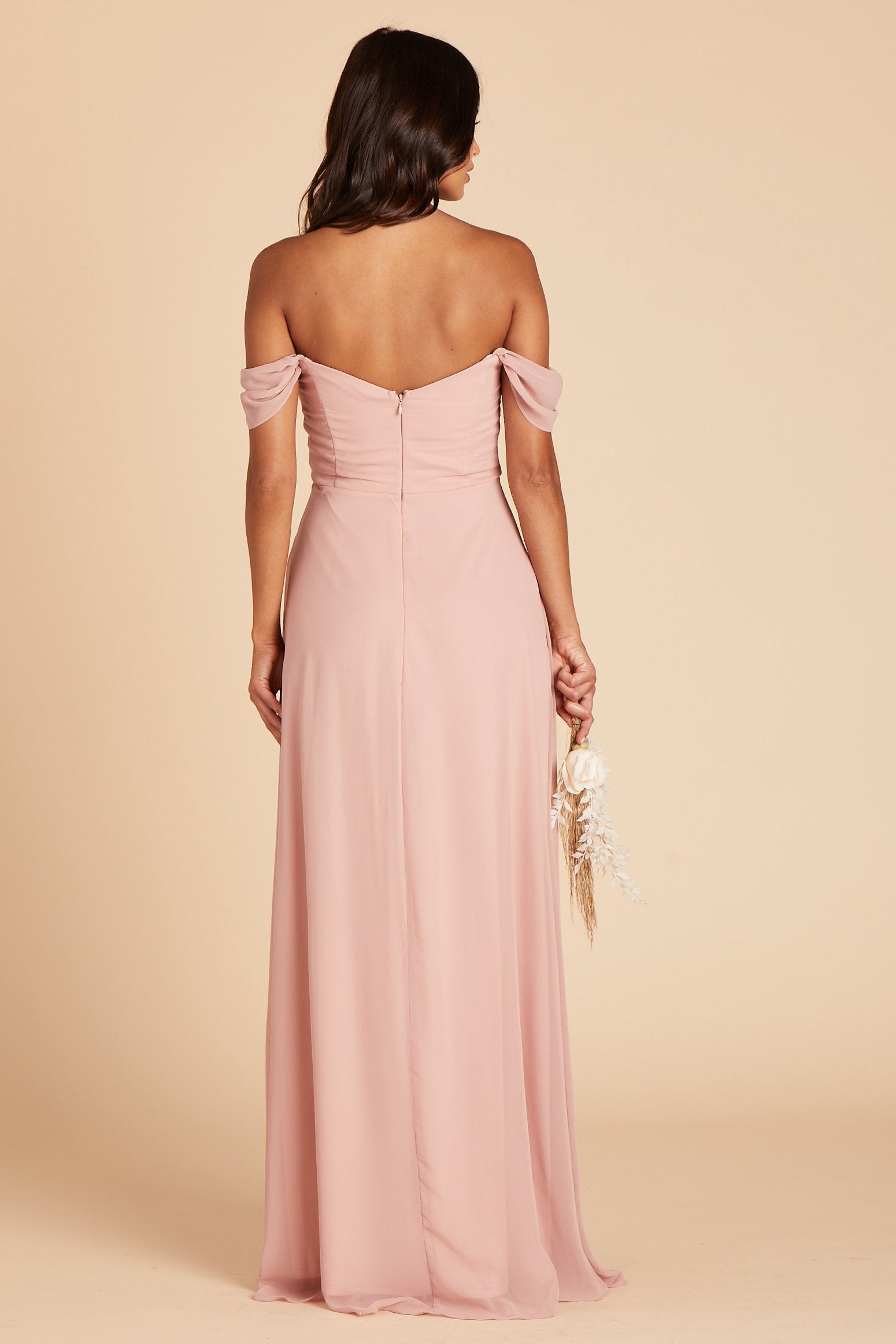 Back view of the Spence Convertible Dress without the optional straps in dusty rose chiffon shows the gentle flow of the shoulder sleeves, the hook and eye closure, and zipper in the center seam of the bodice and dress. The dress conforms to their body along the back and flaring slightly to the floor.