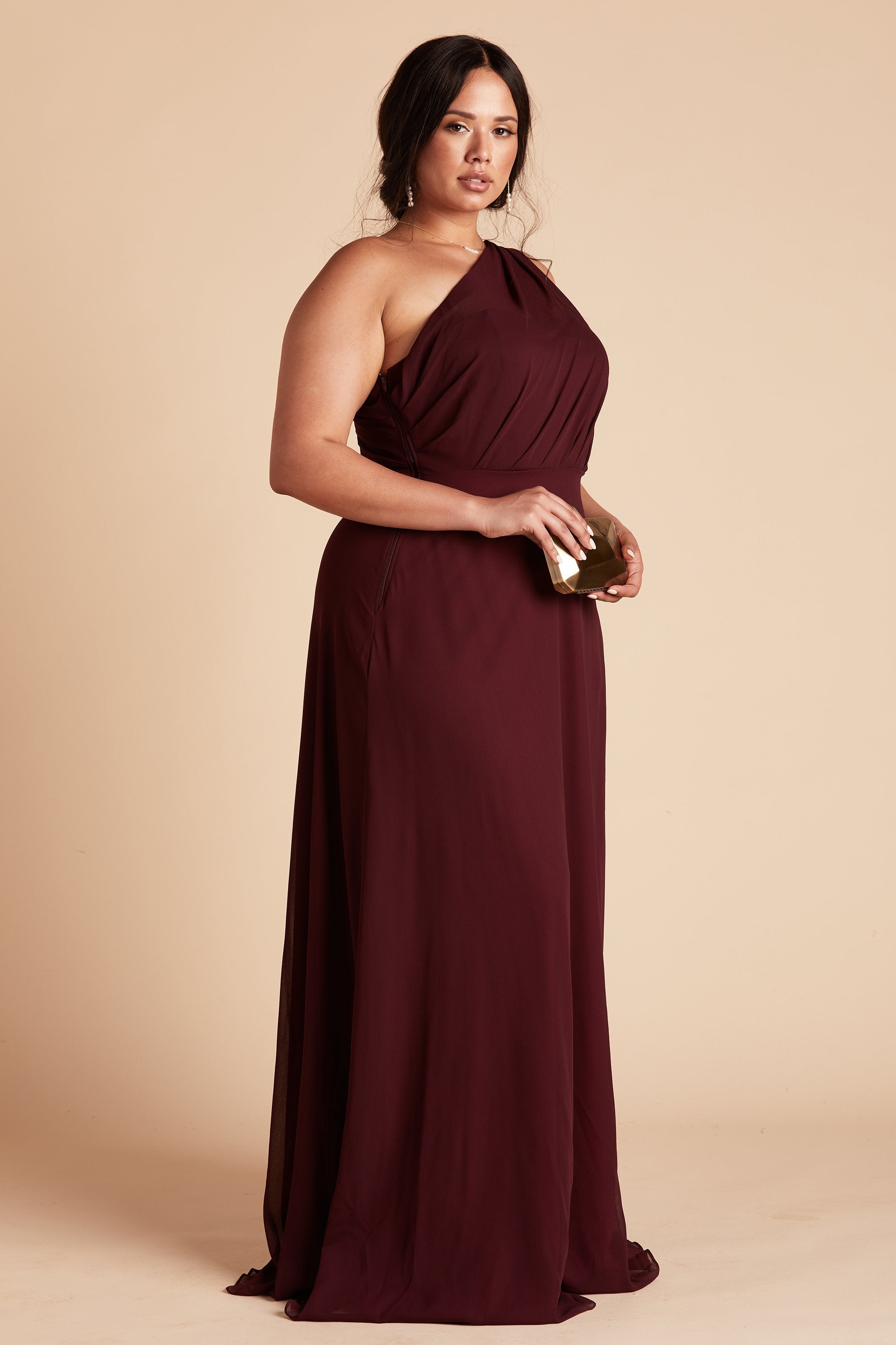 Side view of the Kira Dress Curve in cabernet chiffon without the optional slit shows a full-figured model with a medium skin tone and the dress side seam zipper.