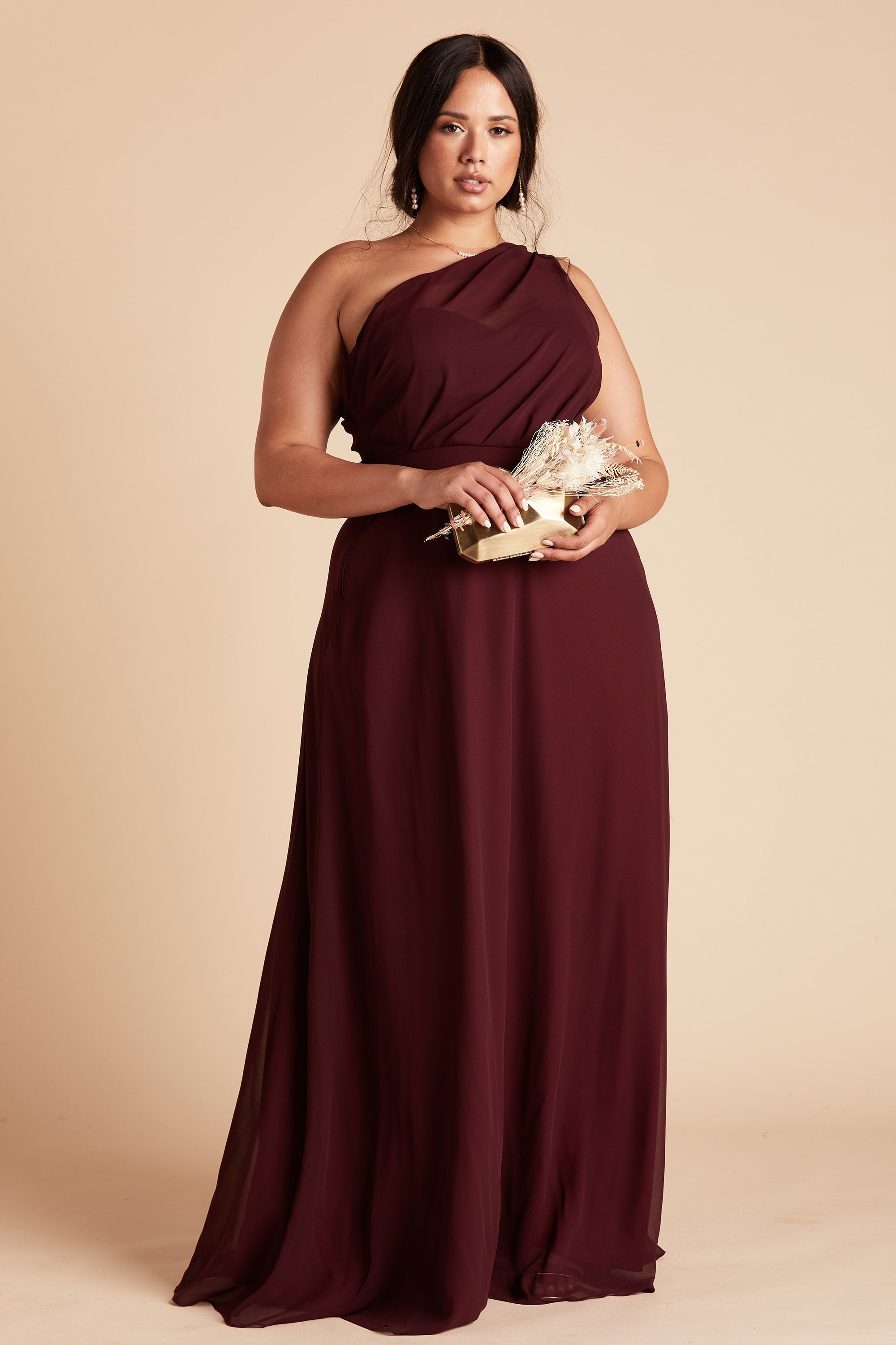 Front view of the Kira Dress Curve in cabernet chiffon without the optional slit shows a full-figured model with a medium skin tone holding the Clear Clutch with Clear Beads purse.