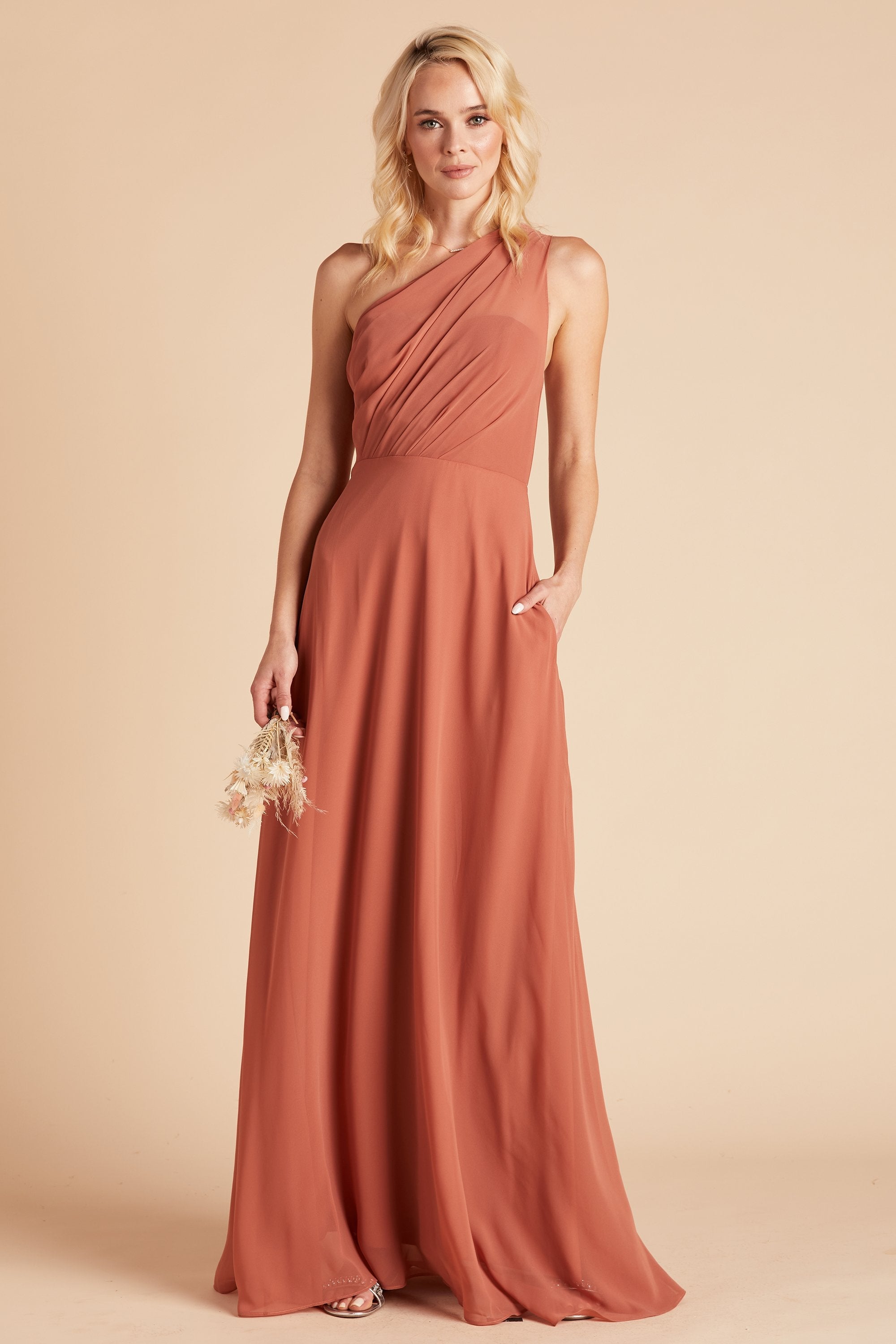 Front view of the Kira Dress in taupe chiffon shows a model with their hand tucked into their left pocket.