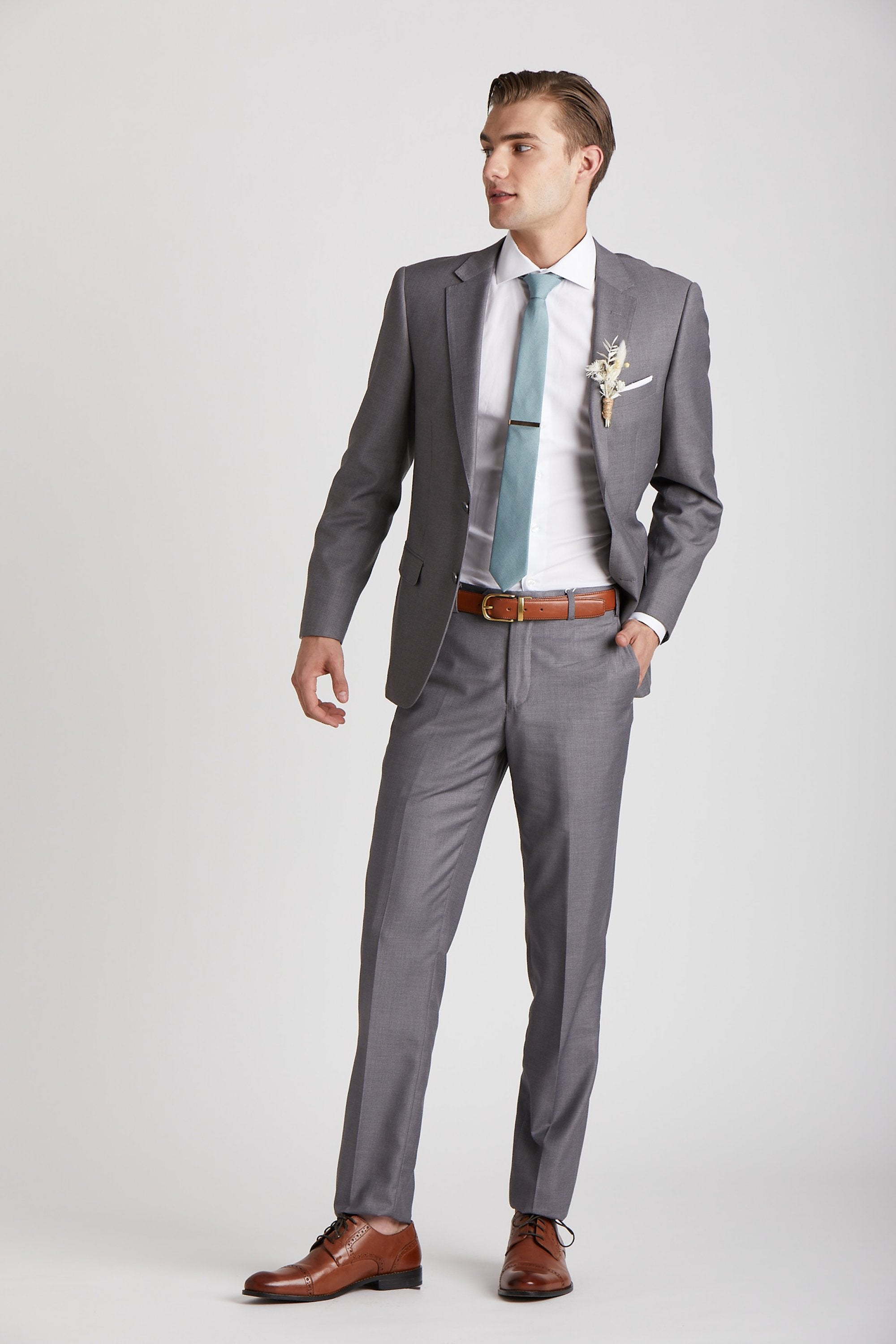 Front view of a model wearing the Simon Necktie in sea glass coordinated with a medium grey suit, white collared shirt, medium brown shoes and belt, and a dried flower boutonniere in ivory. 