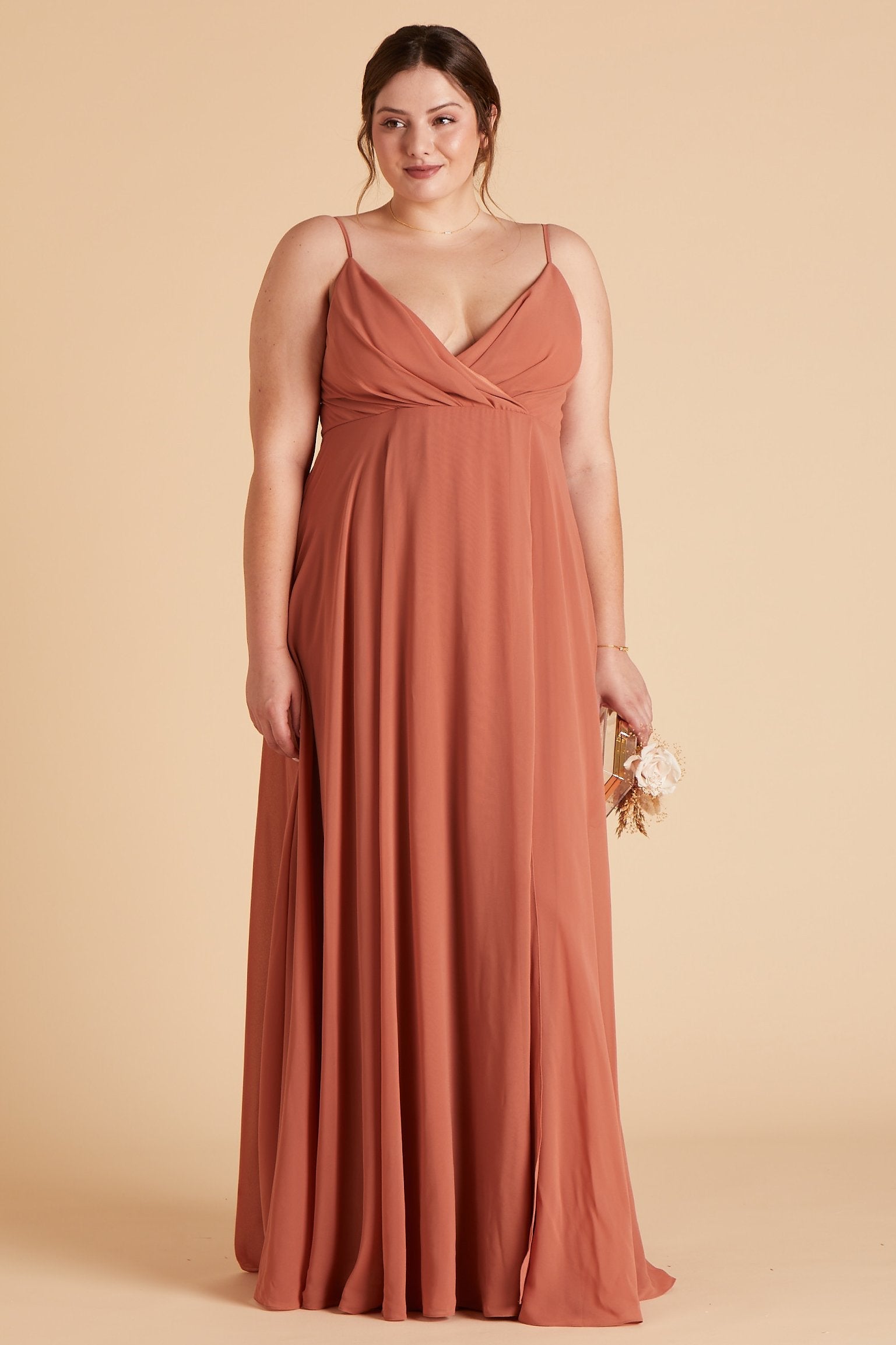 Front view of the floor-length Kaia Dress Curve in terracotta chiffon shows a full-figured model with a light skin tone wearing a spaghetti strap V-neck dress with a raised empire waistline that wraps across their full bosom showing cleavage.