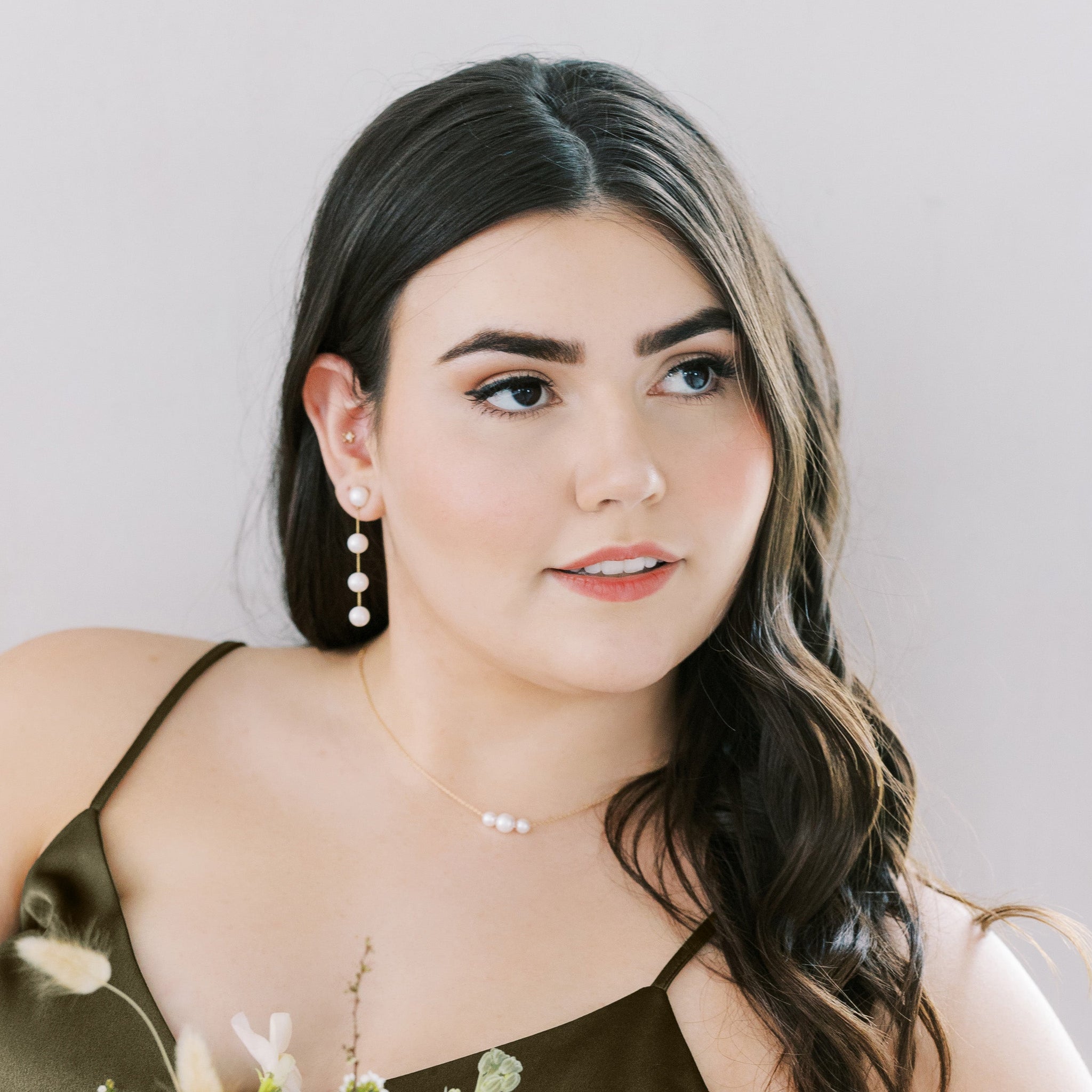 Front view of the Durham Pearl Trio Necklace by Birdy Grey resting above the collarbone of a curvy model with a light skin tone. The necklace is paired with Lowell Pearl Drop Earrings by Birdy Grey.