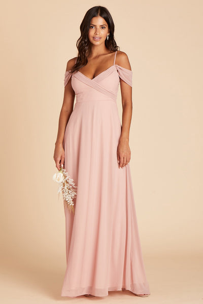 Front view of the Spence Convertible Dress in dusty rose chiffon shows a slender model with a medium skin tone wearing a floor length A-line dress with spaghetti straps and off the shoulder sleeves. The V-neck bodice is high waisted and crisscrosses over the bosom with small pleats along the bodice top.