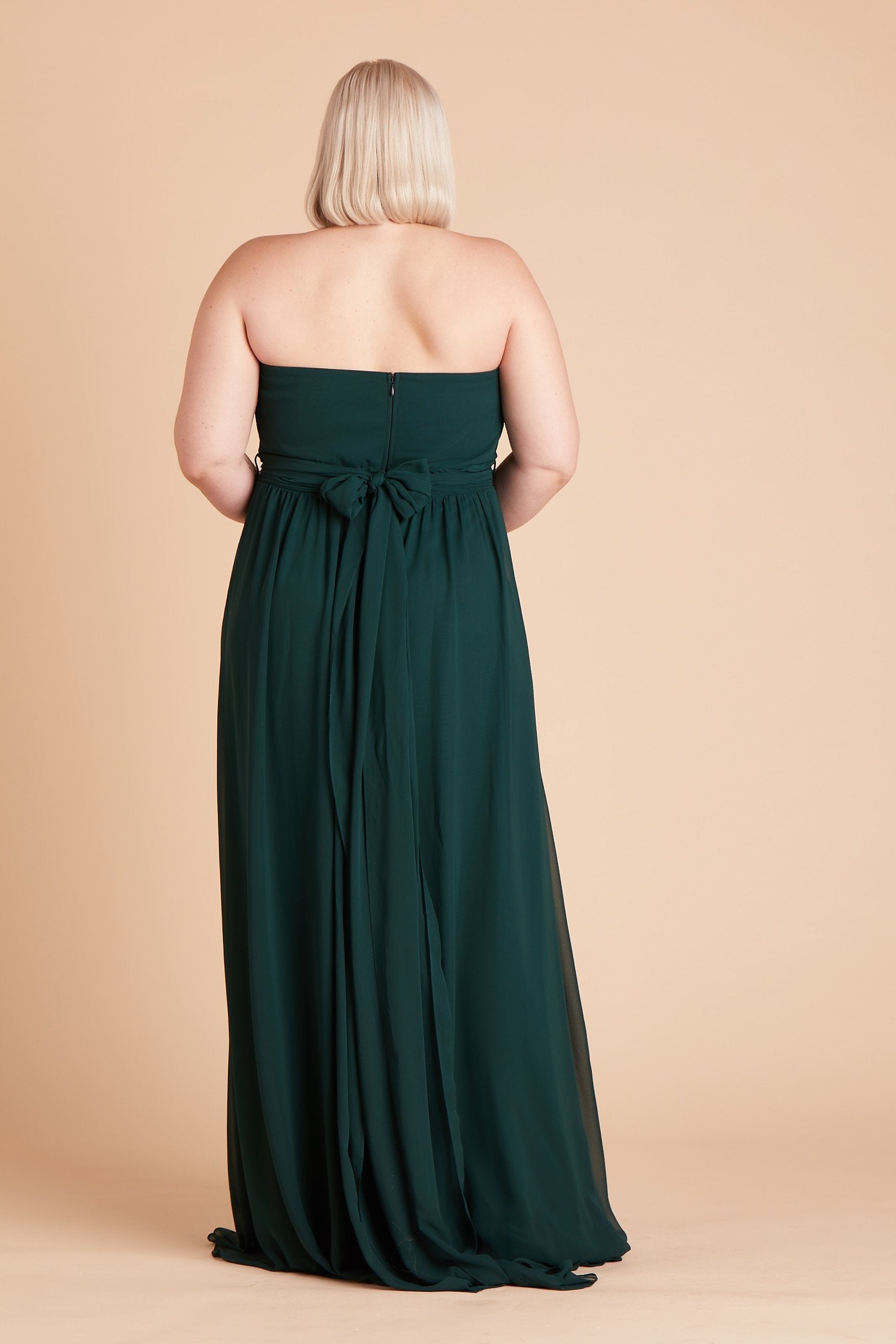 Back view of the Grace Convertible Plus Size Bridesmaid Dress in emerald chiffon reveals an open back cut below the shoulder blades with front streamers tied around the waist in a delicate and flowing bow.