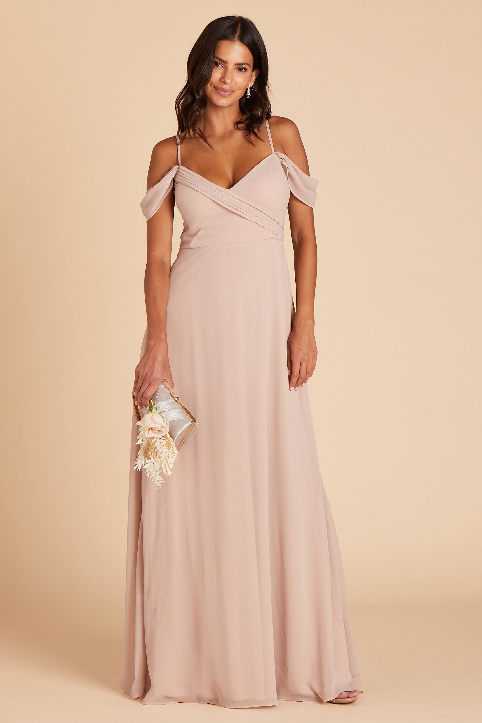 Front view of the Spence Convertible Dress in taupe chiffon shows a slender model with a medium skin tone wearing a floor length, A-line dress with sweeping skirt with spaghetti straps and off the shoulder sleeves. The V-neck bodice is high waisted and crisscrosses over the bosom with small pleats along the bodice top.