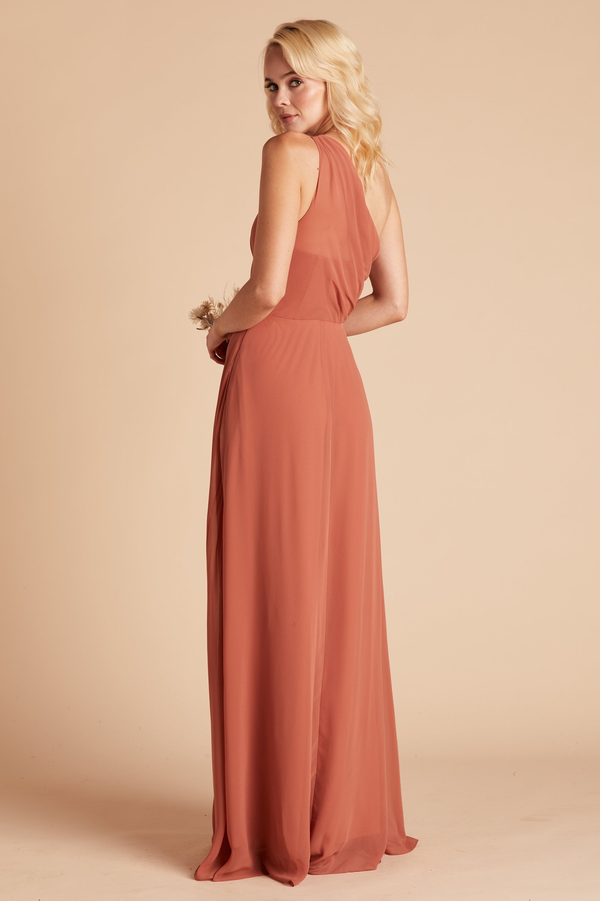 Back and side view of the floor-length Kira Dress in terracotta chiffon of a slender model with a light skin tone showing the soft pleating gathered at the back bodice shoulder and a smooth, conformed fit at the waist.