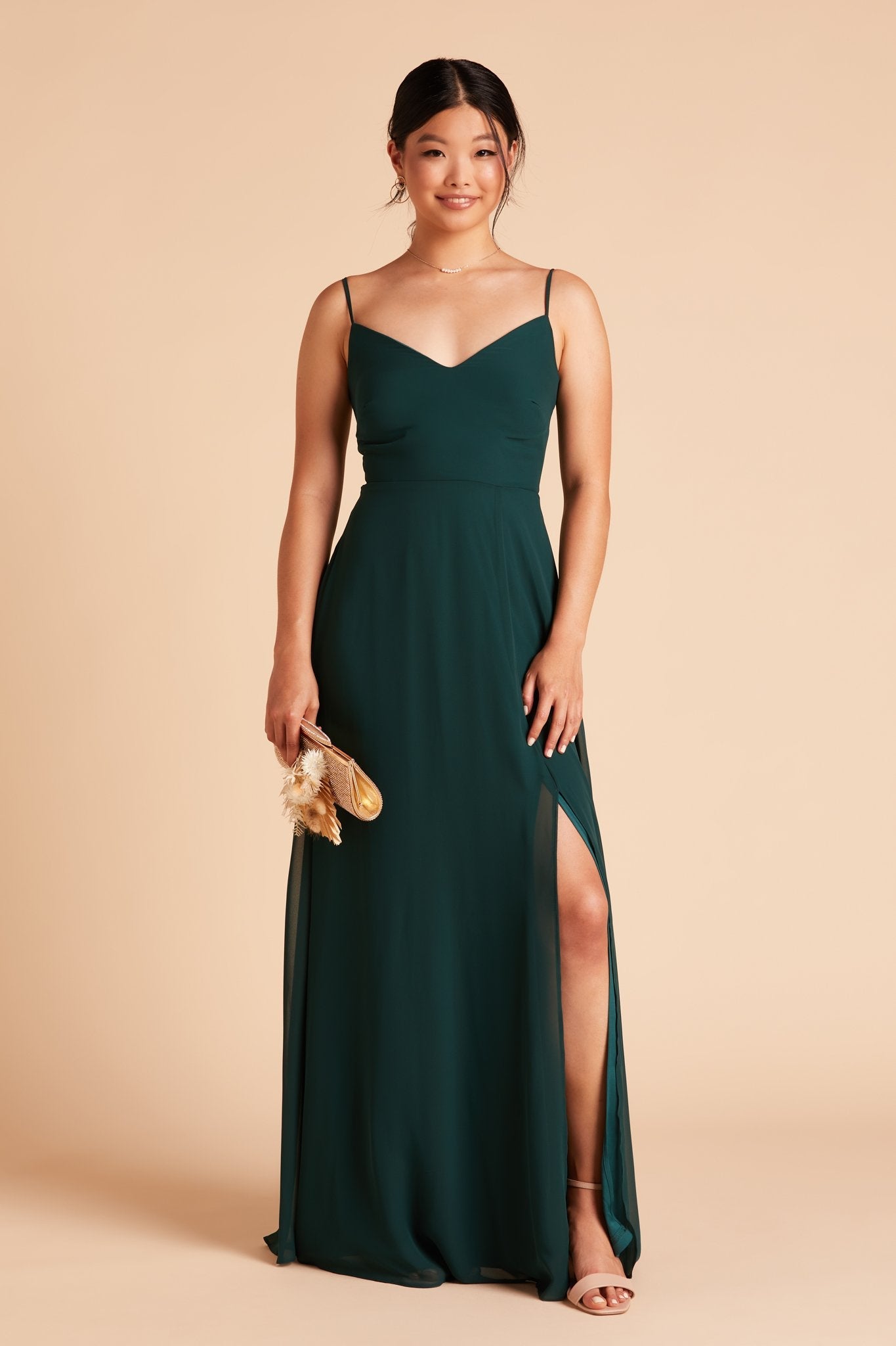 Front view of the floor-length Devin Convertible Bridesmaid Dress in emerald with a flowing skirt features the optional slit over the front left leg.
